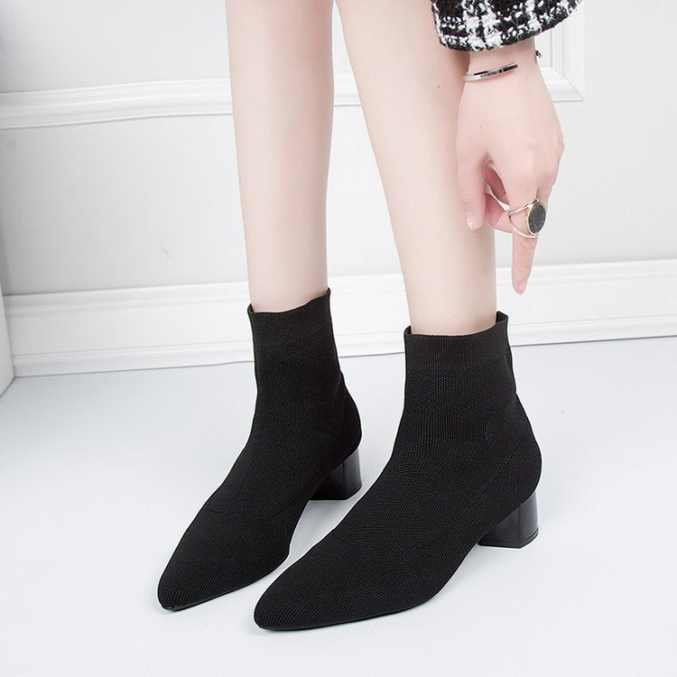 Woman pulling on black sock ankle boots with low block heels