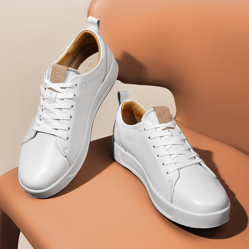Pair of men's white leather low-top court sneakers on a tan chair