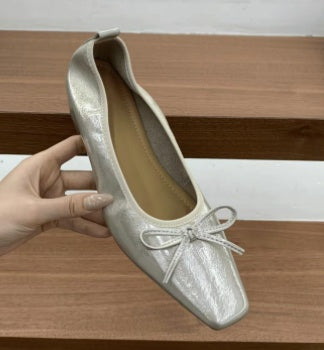 Silver square-toe ballet flat with a bow detail held in hand