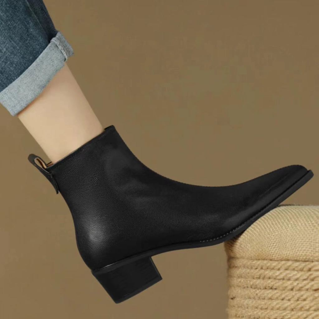Black pointed-toe ankle boot worn with cuffed jeans, side view of the low block heel
