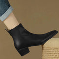 Black pointed-toe ankle boot worn with cuffed jeans, side view of the low block heel