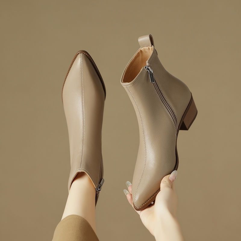 Hand holding a pair of beige pointed-toe ankle boots, showing the inside zip and low stacked heel