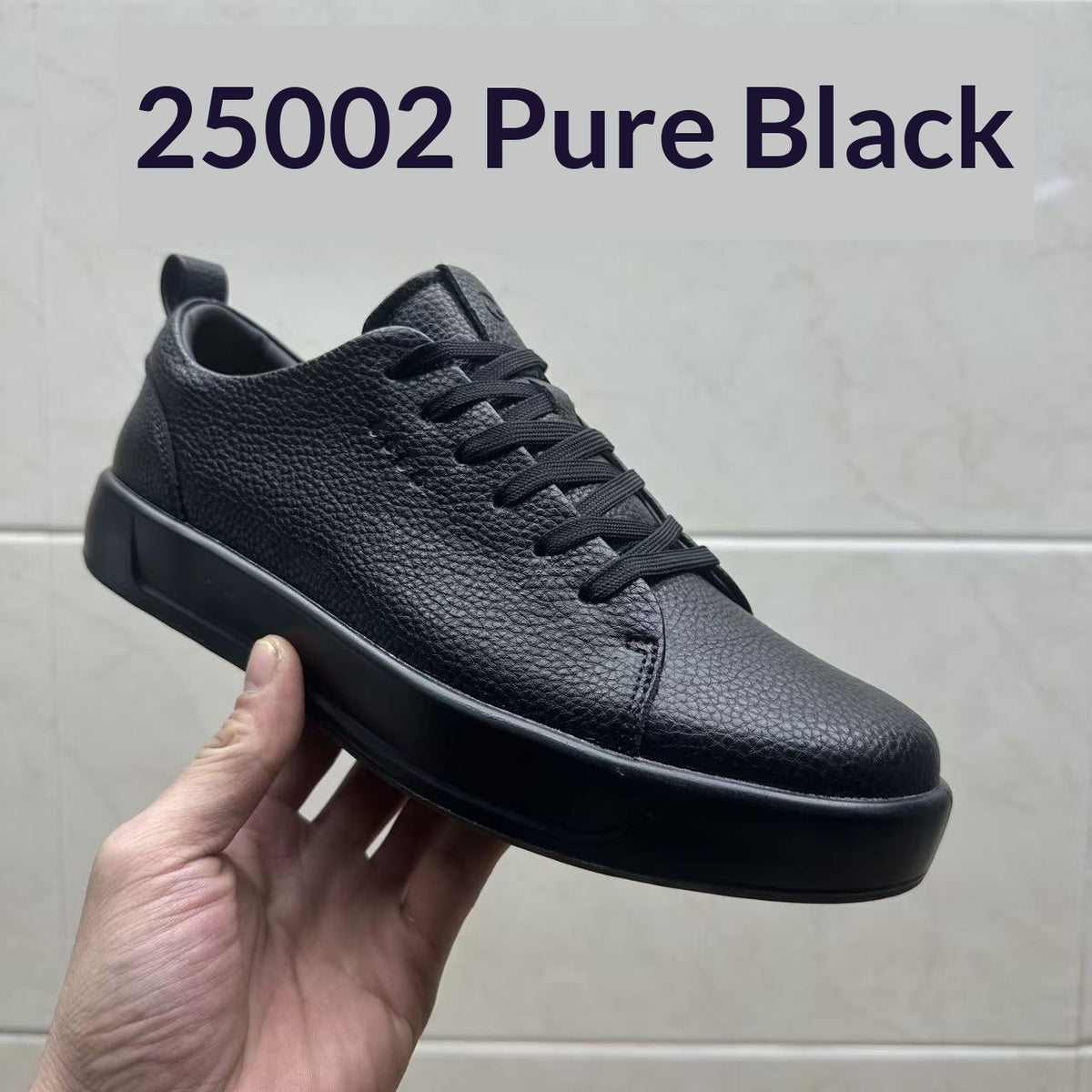 Hand holding a black pebbled leather low-top sneaker