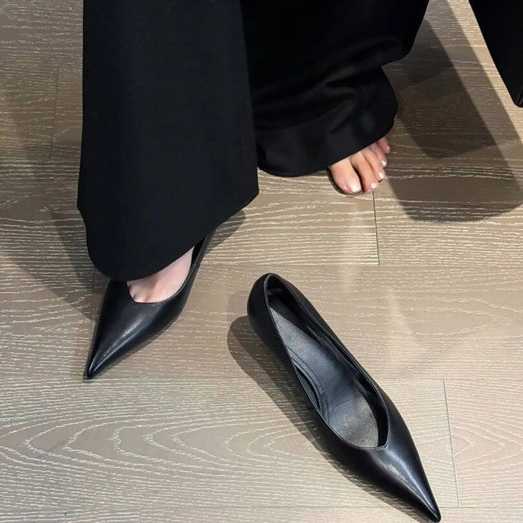 Black pointed low-heel pump on foot beside a second pump on a wood floor