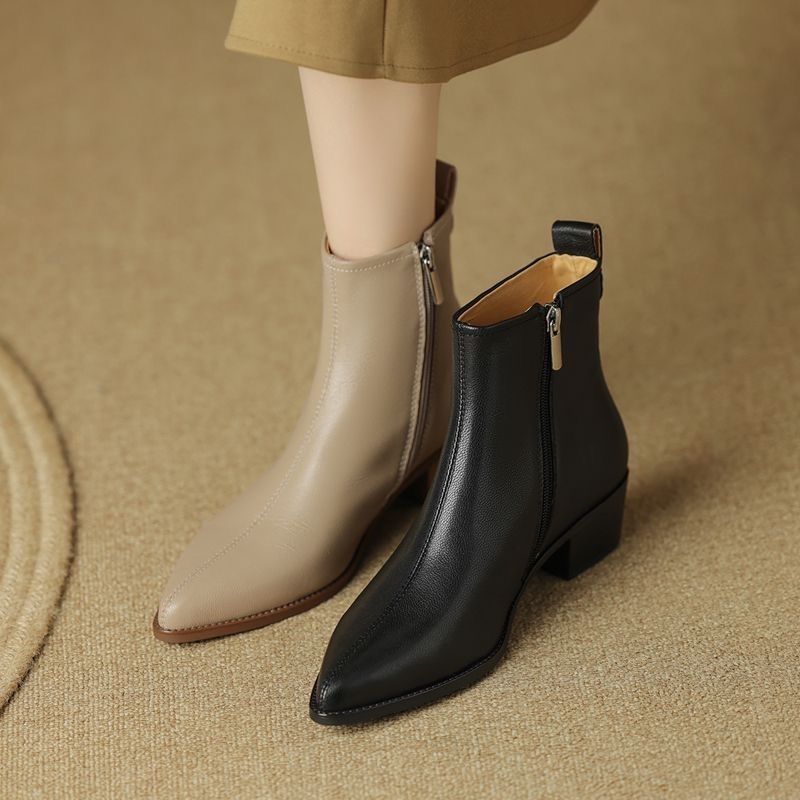 Beige and black pointed-toe ankle boots worn side by side on a woven rug