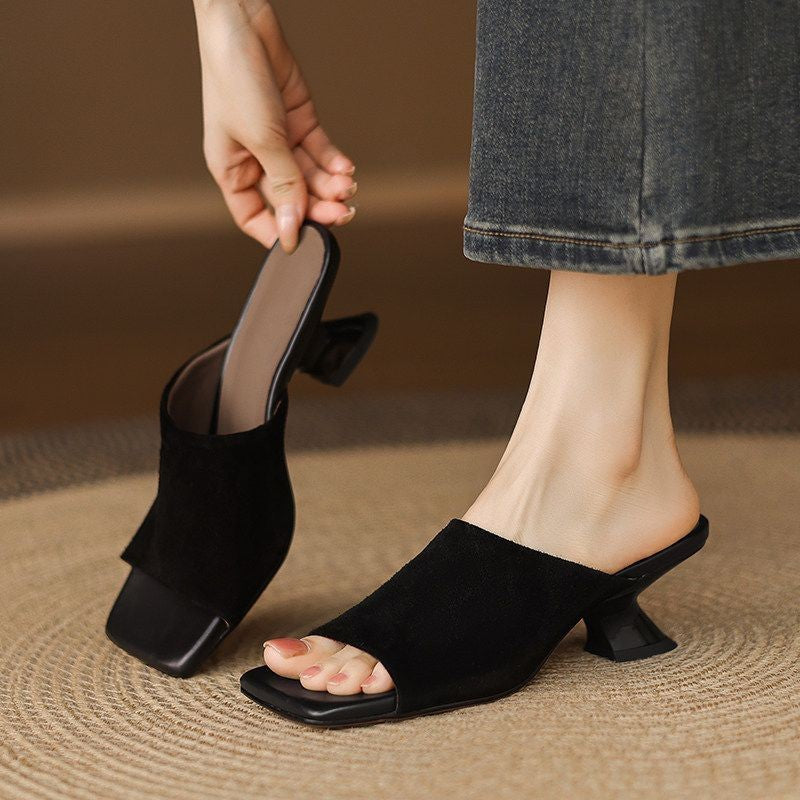 Woman slipping on black suede mules with sculpted heels