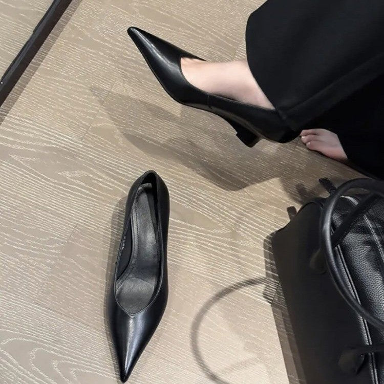 Black pointed low-heel pumps, one on foot and one on the floor, top view