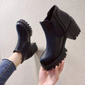 Pair of black Chelsea ankle boots with lug soles held in hand