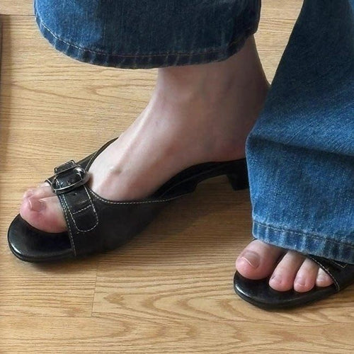 Woman wearing black buckle mules, front view