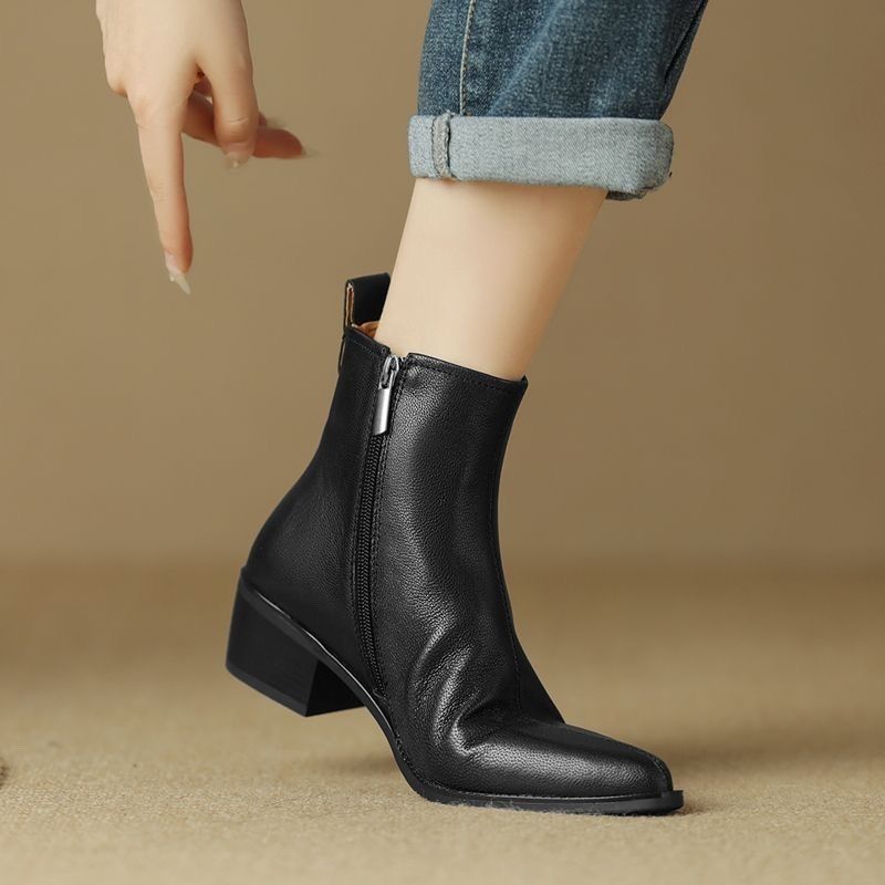 Woman wearing a black pointed-toe ankle boot with side zip and cuffed jeans