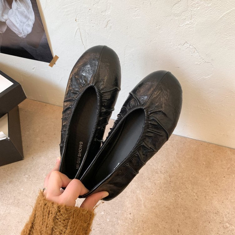 Hand holding black pleated round-toe ballet flats